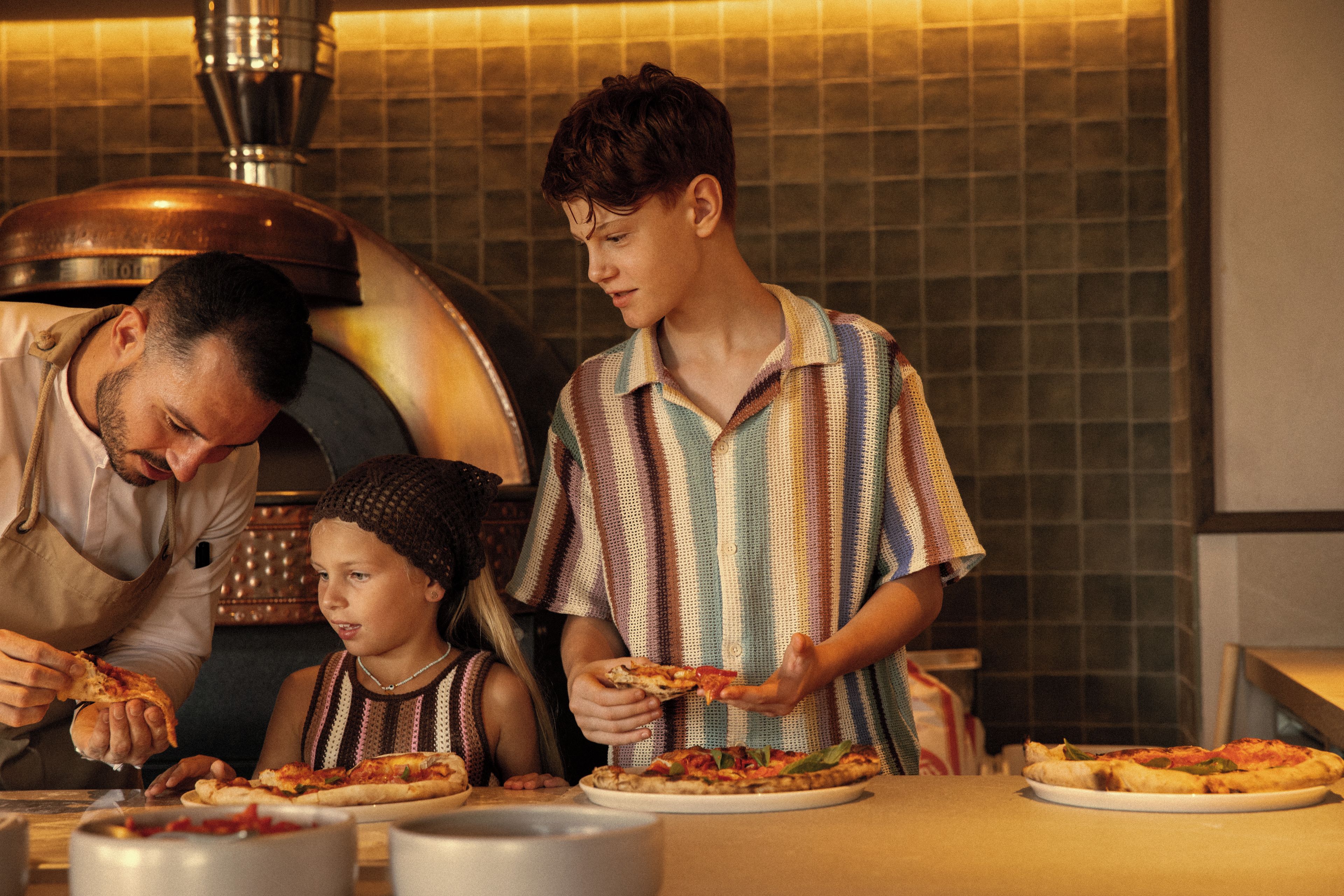 A family preparing and serving pizza in a kitchen with a large pizza oven.