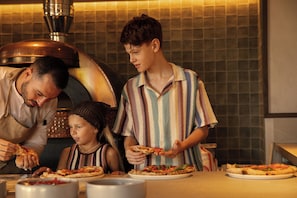 A family preparing and serving pizza in a kitchen with a large pizza oven. - Ikos Kissamos - All Inclusive (Kissamos)