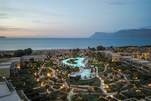 A resort with a central swimming pool, multiple buildings, and a beach in the background.