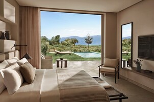 A bedroom with a large bed, a TV, and a view of a pool and mountains.