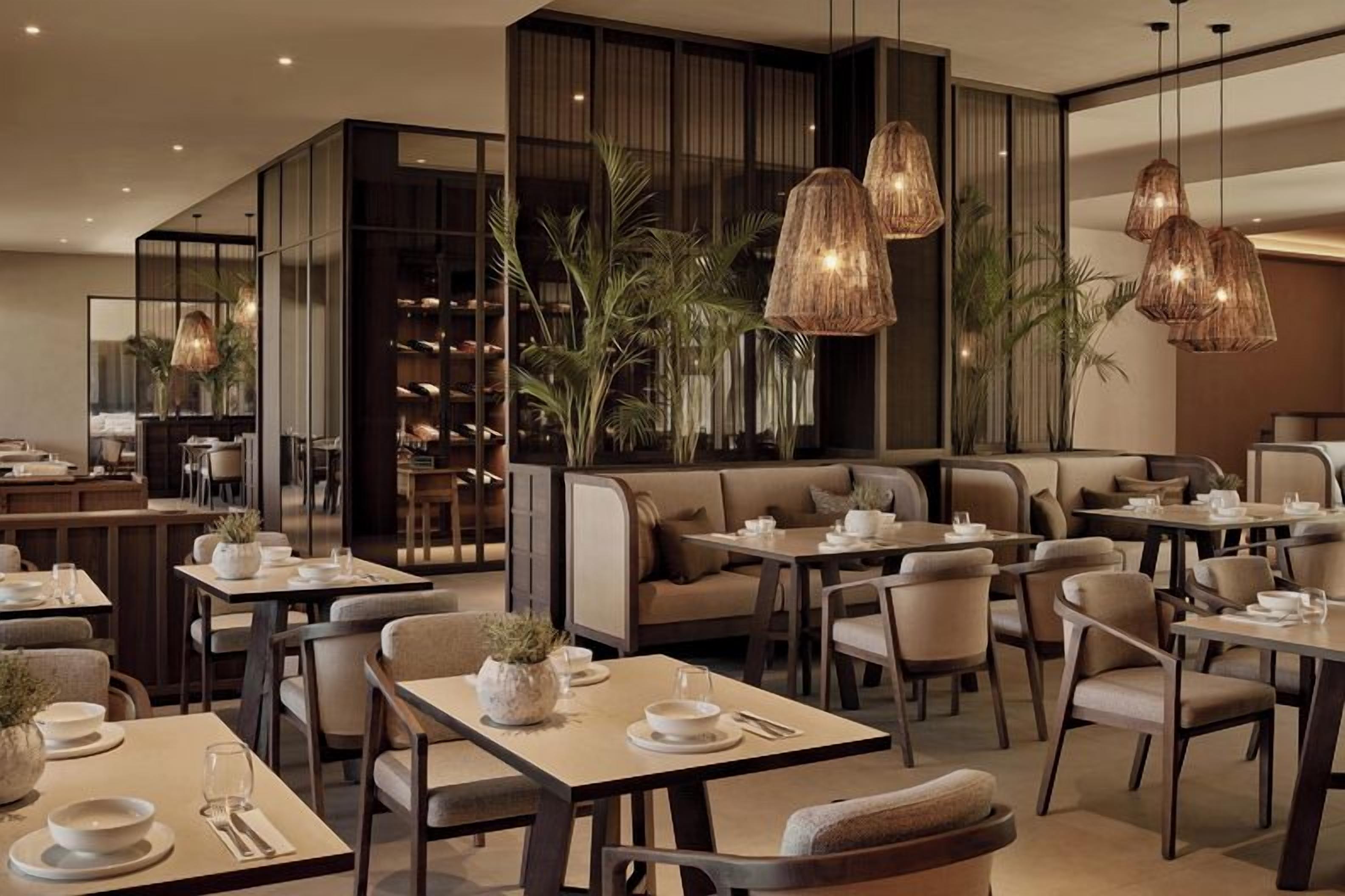A restaurant interior with tables, chairs, hanging light fixtures, and a bookshelf.