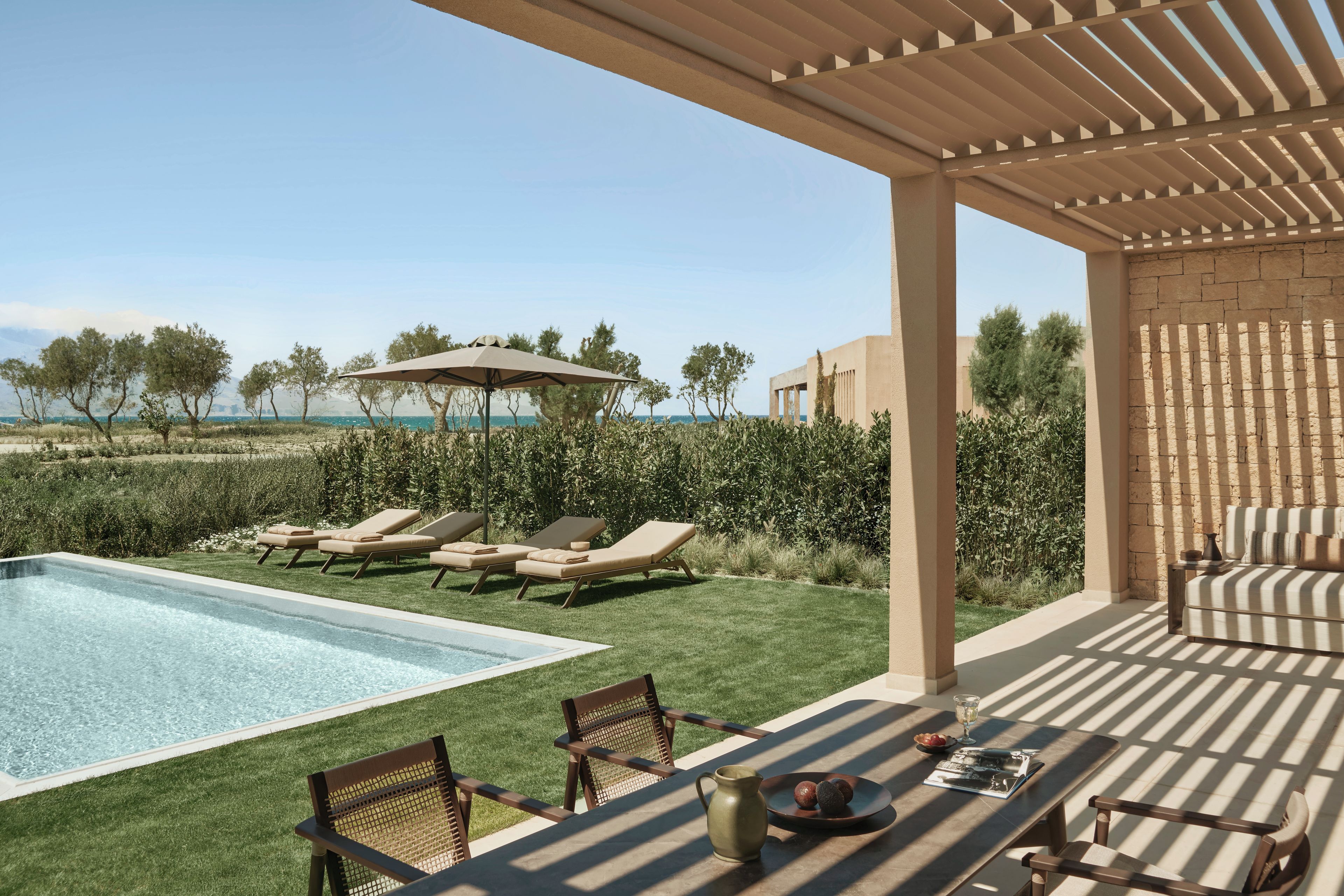 A poolside area with lounge chairs, a table with a pitcher and snacks, and a pergola with an umbrella.