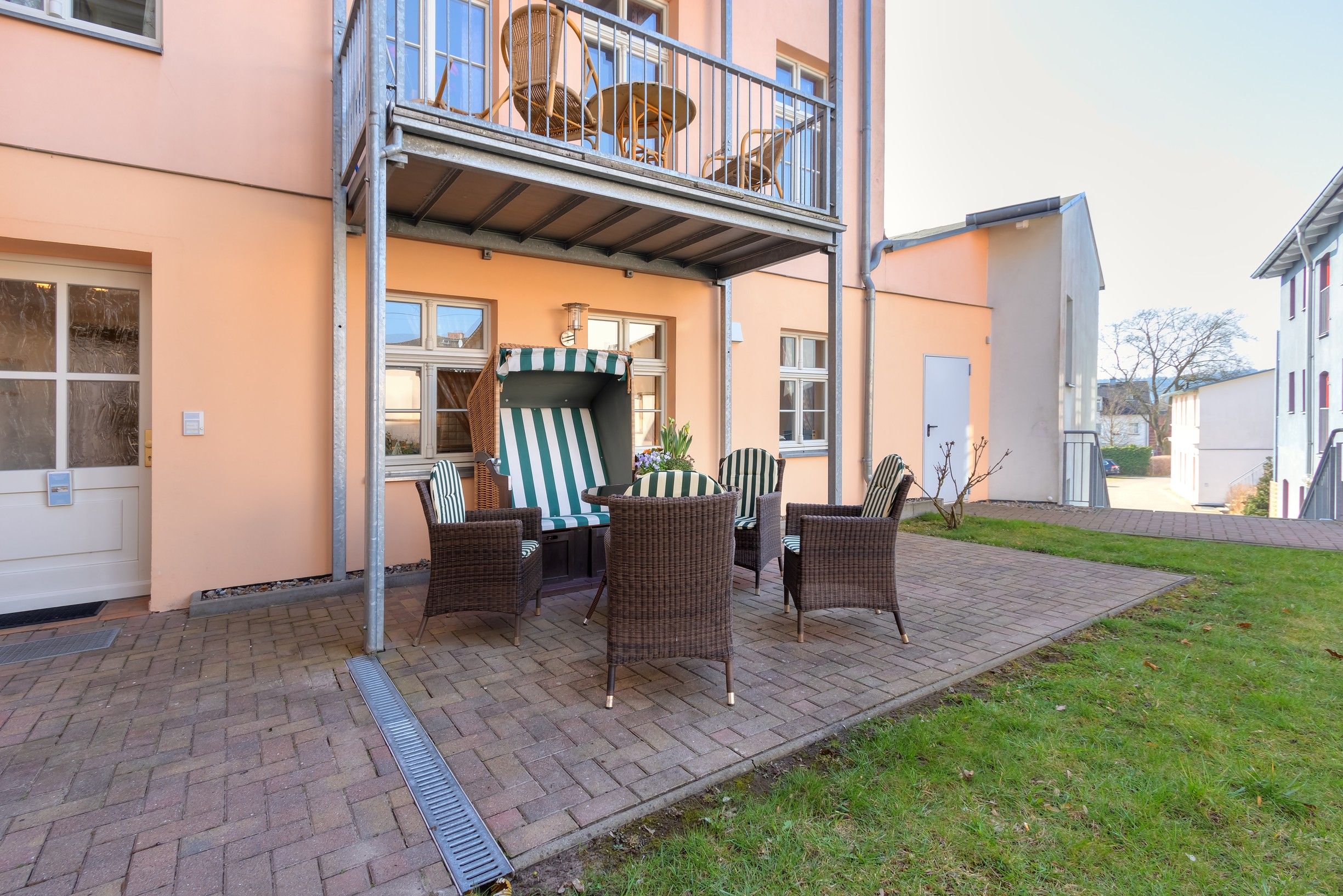 Ein zweistöckiges Gebäude mit einem Balkon, Korbmöbeln und einem Ziegelweg.