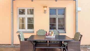 Eine Terrasse im Freien mit Tisch, Korbstühlen, einer Weinflasche und einem Blumenstrauß.