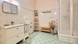 A bathroom with a white vanity, a mirror, a towel rack, a shelf with toiletries, a bench, and a shower area.