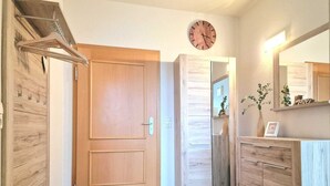 A hallway with wooden flooring, a wooden door, a mirror, and a clock on the wall.