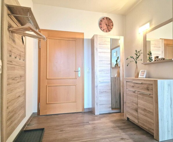 A hallway with wooden flooring, a wooden door, a mirror, and a clock on the wall. - Bella Vita vacation apartment in Trassenheide - sea views for the whole family (Trassenheide)