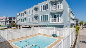 A multi-story building with balconies, a swimming pool, and a white fence. - 1BR Beach Retreat - Pool, Parking & Boardwalk (Ocean City)