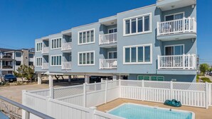 A multi-story building with balconies, a pool, and a sign indicating sales, rentals, and services. - 1BR Beach Retreat - Pool, Parking & Boardwalk (Ocean City)