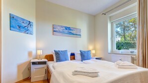 A hotel room with a large bed, two bedside tables with lamps, a window with a view of trees, and two paintings on the wall. - House Berlin, apartment Loddiner Höft in Loddin - in the best location near the Achterwasser (Loddin)