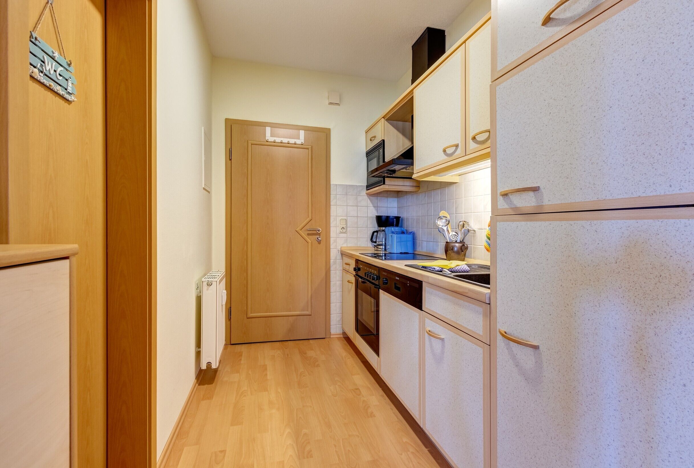Eine schmale Küche mit Holzschränken, einem weißen Kühlschrank und einem Herd.
