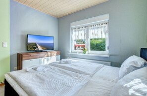Relax in a spacious room with a large bed, flat-screen TV, and a window with white curtains.