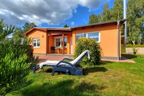 Guests can enjoy a patio area with a table and chairs, surrounded by a well-maintained lawn and lush greenery.