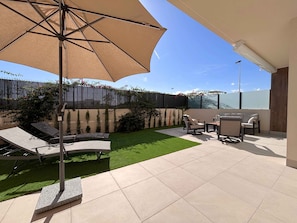 Une terrasse extérieure avec un parasol, des chaises longues, une petite pelouse et une vue sur la ville.