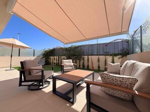 Une terrasse avec des meubles d’extérieur, une table et un grand parasol.