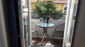 Uma varanda com porta de vidro, uma mesa redonda com duas cadeiras, uma garrafa de vinho e um copo de vinho.