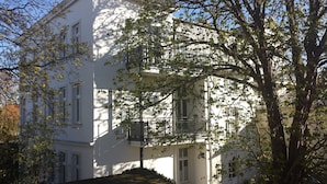 A white multi-story building with balconies, surrounded by trees and a paved area. - Villa Bismarckshöhe, Alma apartment in the Baltic seaside resort of Ahlbeck - 4-star Baltic Sea vacation (Ahlbeck)