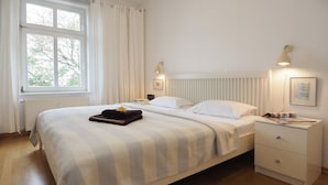 A neatly made bed with a striped blanket, a bedside table with a lamp, and a window with curtains. - Villa Bismarckshöhe, Alma apartment in the Baltic seaside resort of Ahlbeck - 4-star Baltic Sea vacation (Ahlbeck)