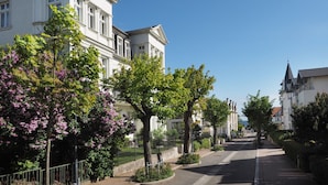 A street lined with white buildings, trees with purple flowers, and a clear blue sky. - Villa Bismarckshöhe, Alma apartment in the Baltic seaside resort of Ahlbeck - 4-star Baltic Sea vacation (Ahlbeck)