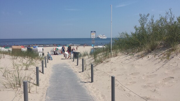 A sandy beach path leading to the sea with beach umbrellas and a lifeguard tower. - Villa Bismarckshöhe, Alma apartment in the Baltic seaside resort of Ahlbeck - 4-star Baltic Sea vacation (Ahlbeck)