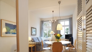 A modern hotel room with a round dining table, striped sofa, and a large window with curtains. - Villa Bismarckshöhe, Alma apartment in the Baltic seaside resort of Ahlbeck - 4-star Baltic Sea vacation (Ahlbeck)