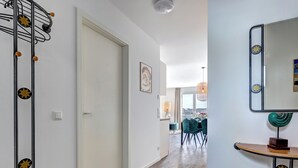 Un pasillo con suelo de madera, un comedor con sillas y una mesa, y un espejo en la pared.