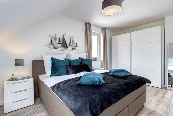 Une chambre moderne avec un grand lit, une table de chevet, un luminaire fixé au mur et une fenêtre avec des rideaux.