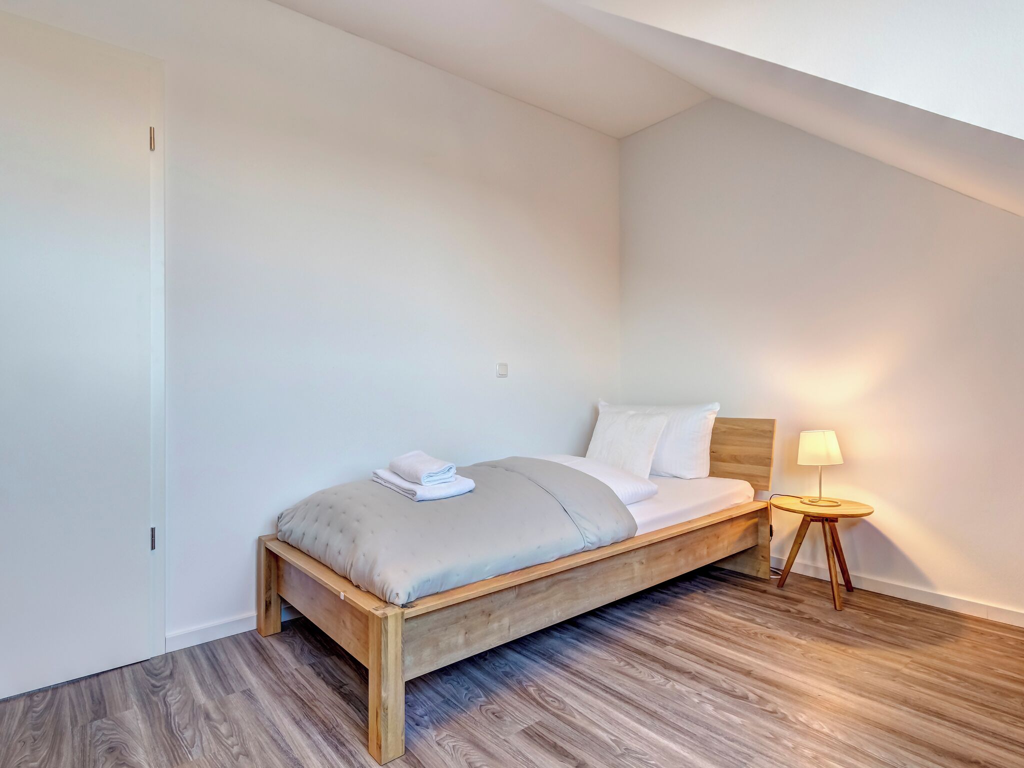 A bedroom with a wooden bed, a nightstand with a lamp, and a wooden floor.