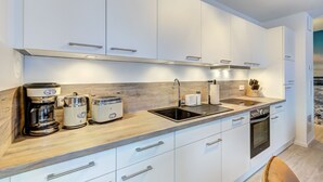 A modern kitchen with white cabinets, a wooden countertop, a built-in oven, and a coffee maker.