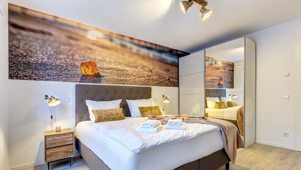 A modern bedroom with a large bed, bedside lamps, a wooden nightstand, and a mirror.