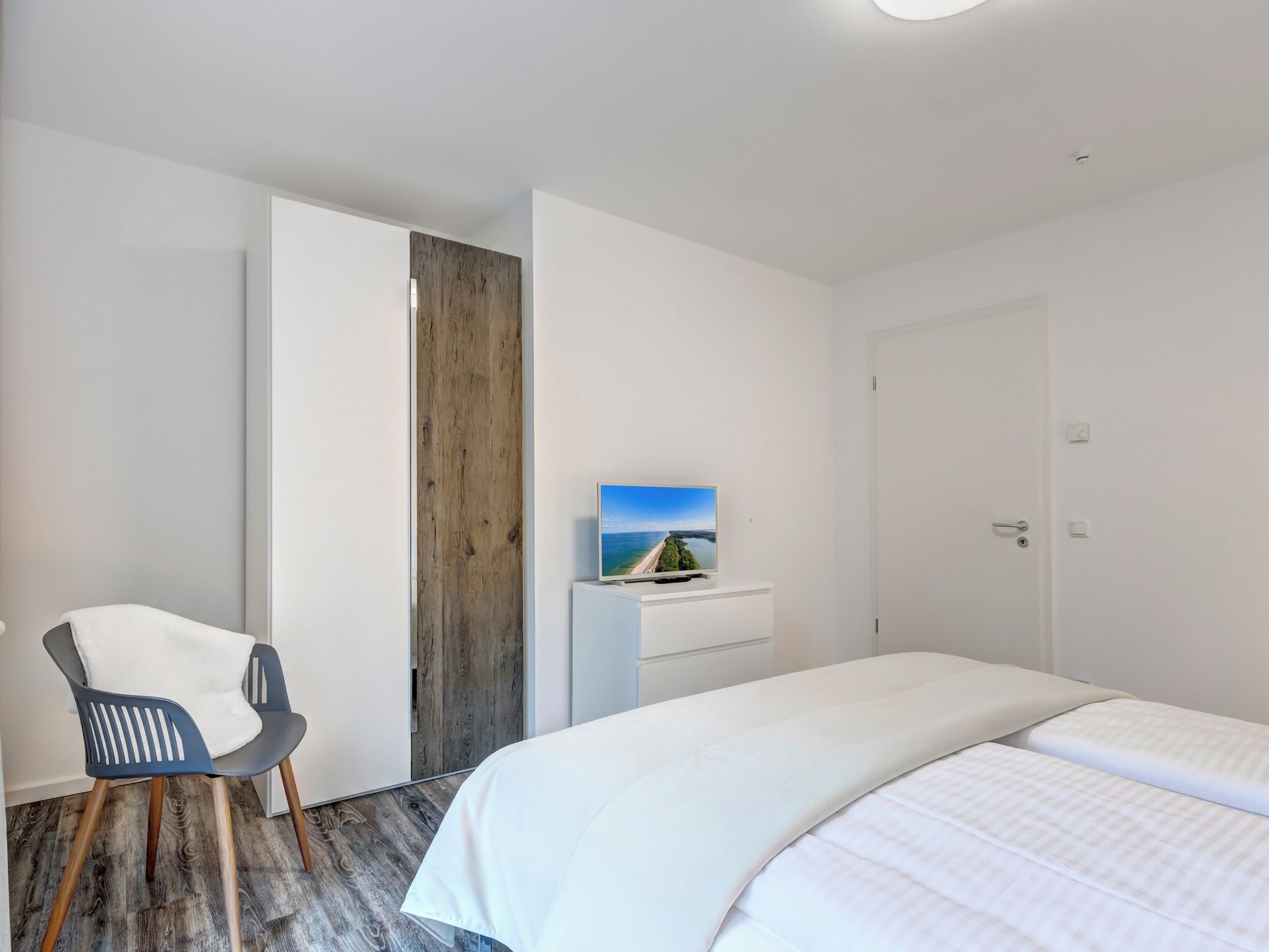 A modern hotel room with a bed, a desk with a flat-screen TV, a chair, and a wooden accent wall.