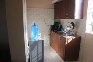 Kitchen area with refrigerator, sink, and cabinets, featuring a tiled backsplash and window.