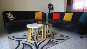 Een woonkamer met een zwart hoekbank, twee ronde tafels met gouden poten en een kamerbreed tapijt.