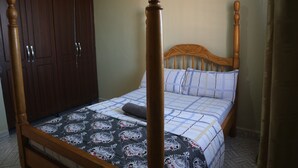Een slaapkamer met een houten baldakijnbed, een nachtkastje en een garderobe.