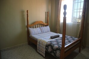 Un lit à baldaquin en bois, recouvert d’une couverture à carreaux et d’une couverture pliée.