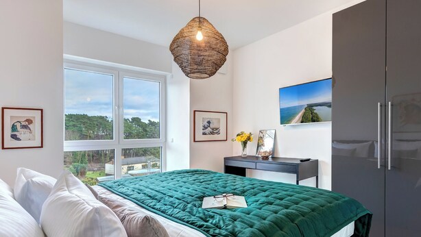 A modern bedroom with a large bed, a desk with a computer, and a wardrobe.