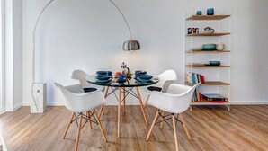 A modern dining area with a round glass table, white chairs, a metal lamp, and a wooden floor.