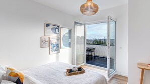 A bedroom with a bed, a bedside table, a hanging light fixture, and a view through a glass door to an outdoor balcony.