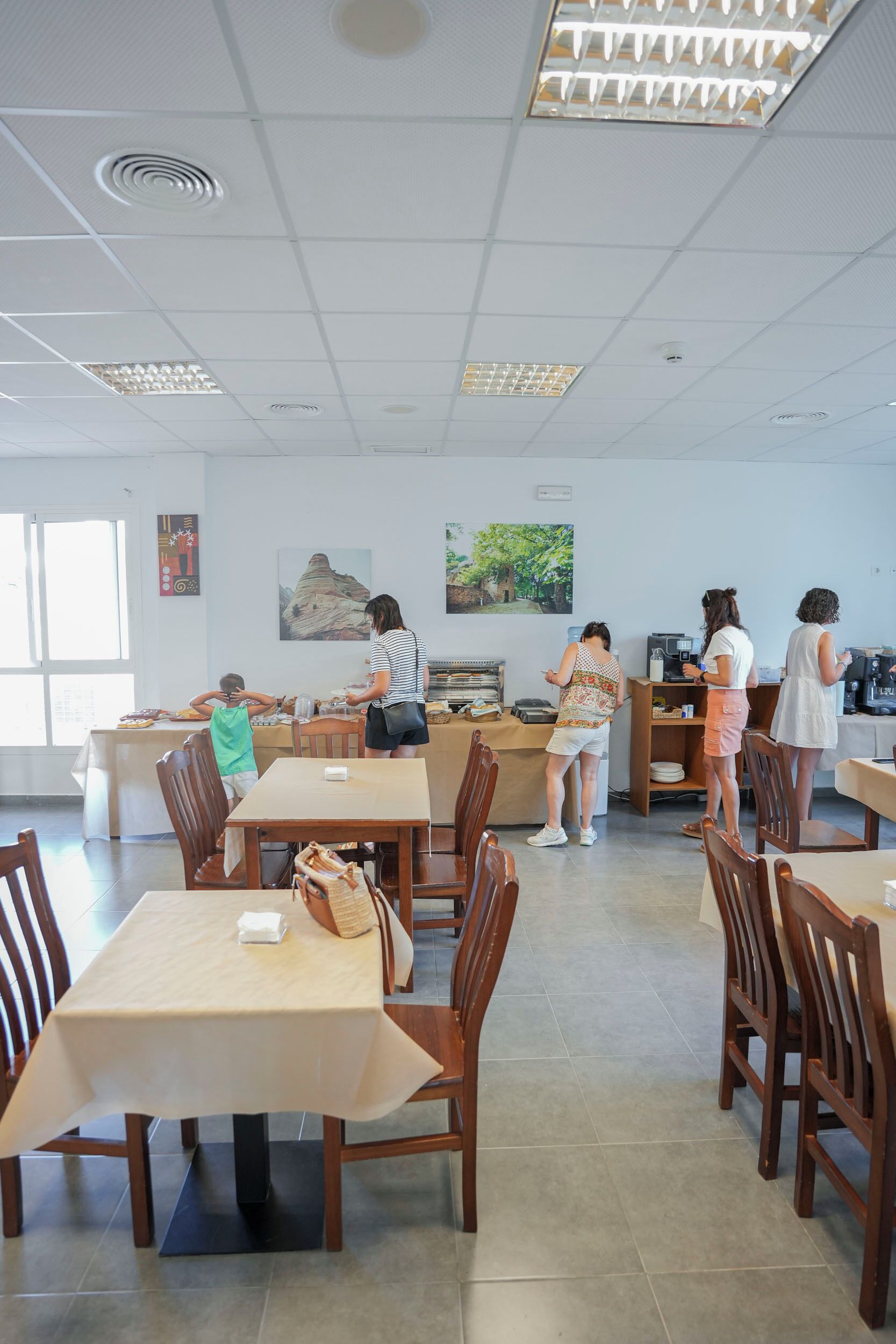 Un comedor amplio con múltiples mesas y sillas, una barra de servicio y obras de arte en las paredes.