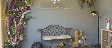 A modern interior with a decorative floral arrangement, a cushioned bench, a glass coffee table, and a bookshelf.