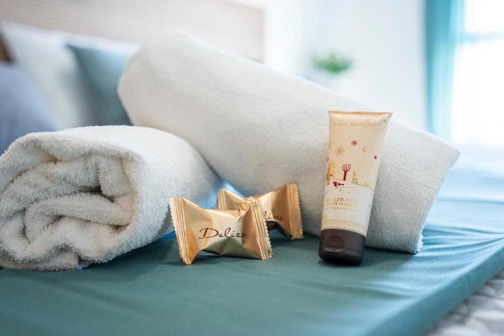 A neatly folded white towel, a tube of cream, and two small packets on a teal bedspread.