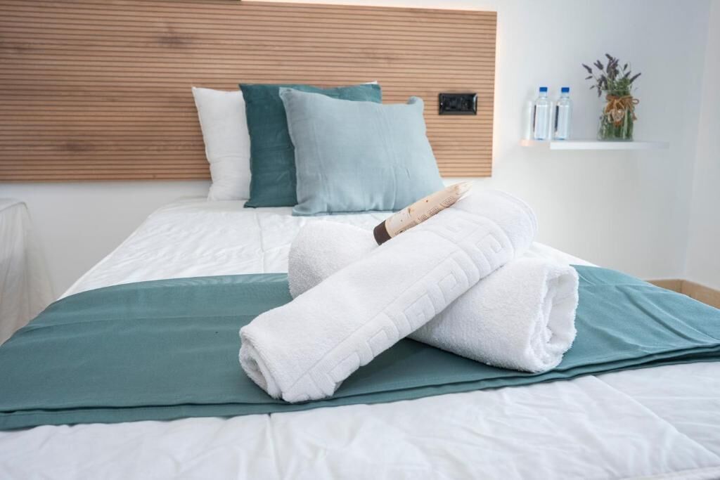 Una cama bien hecha con ropa de cama blanca y turquesa, una toalla doblada y un cabecero de madera.