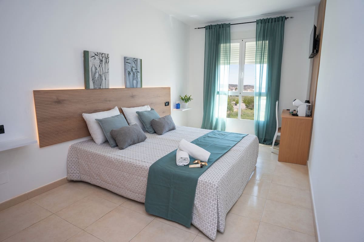 Een moderne slaapkamer met een groot bed, een hoofdbord en uitzicht op het groen door een raam met gordijnen.