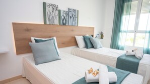 Une chambre d’hôtel avec deux lits, chacun doté d’une tête de lit en bois, de draps blancs et d’éléments de décoration de couleur turquoise. On trouve des serviettes et un petit vase sur les lits.