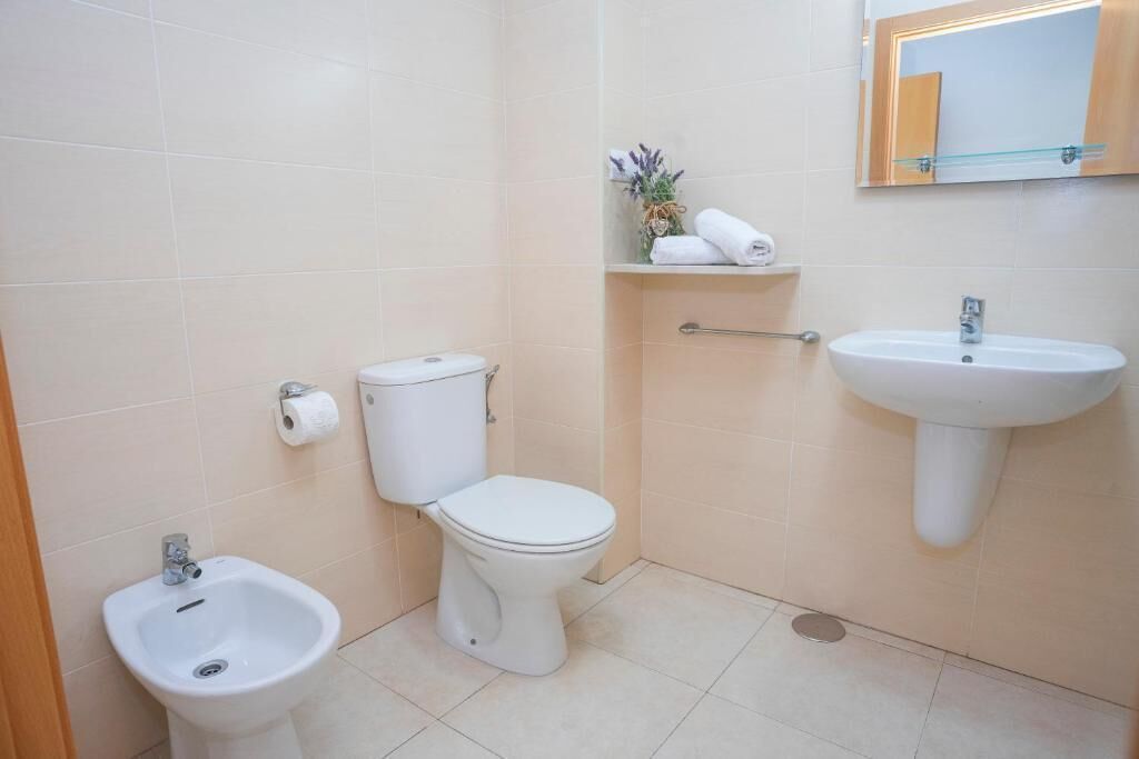 A bathroom with a toilet, bidet, sink, and a mirror on the wall.