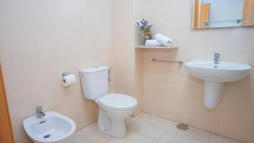 A bathroom with a toilet, bidet, sink, and a mirror on the wall.