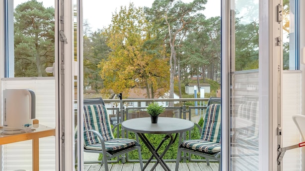 A balcony with a table and chairs, a potted plant, and a view of trees and houses. - Haus Eichhorst, Whg. 03: Close to the sandy beach in Trassenheide (Trassenheide)