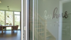 Un intérieur moderne comprenant un coin repas, une porte en verre ornée d’un logo et donnant sur une terrasse en bois.