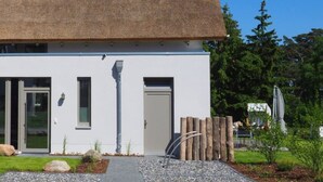 Un bâtiment moderne à la façade blanche, doté d’un toit de chaume et agrémenté d’un petit jardin avec des rochers et des plantes.