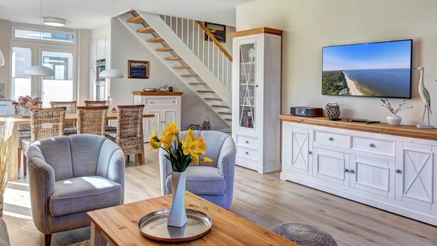 Un vaste salon comprenant une table à manger en bois, deux fauteuils gris, un meuble blanc et un escalier menant à un autre niveau.